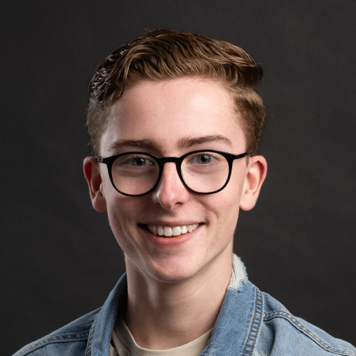 Lachende jongeman met bril op en spijkerjack aan, tegen een zwarte achtergrond